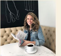 a woman sitting at a table with a book and cup of coffee in front of her