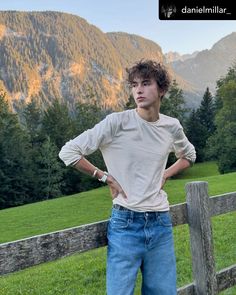 a young man standing in front of a wooden fence with his hands on his hips