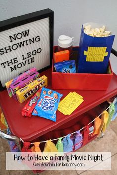 a red table topped with candy bags and movie tickets next to a sign that says now showing the lego movie