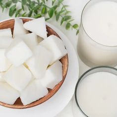 a bowl of sugar cubes next to two glasses of milk on a white table