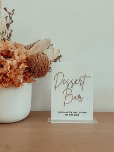 a vase filled with dried flowers next to a sign that reads dessert bar opens after the cuttings of the cake