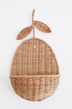 an oval wicker basket hanging on the wall with two leaves attached to it,