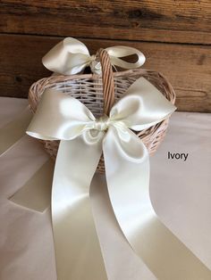 a basket with white satin ribbons tied to it and labeled ivory on the side, sitting on a bed