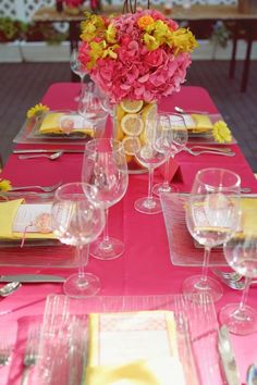 the table is set with pink and yellow plates, silverware, and wine glasses