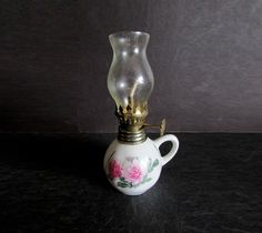 a white vase with pink flowers on it sitting on a table next to a light bulb