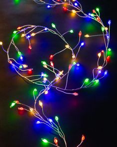 multicolored christmas lights are on the ground in front of a black background,