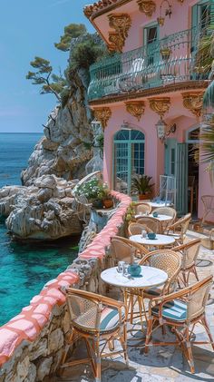 an outdoor dining area with tables and chairs next to the ocean in front of a pink building