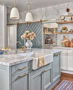 a kitchen with marble counter tops and white cabinets, along with hanging lights above the sink