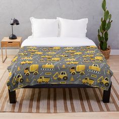 a bed with a yellow and gray construction truck pattern on the comforter next to a potted cactus