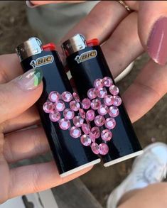 two black lighters with pink flowers on them are being held by someone's hands