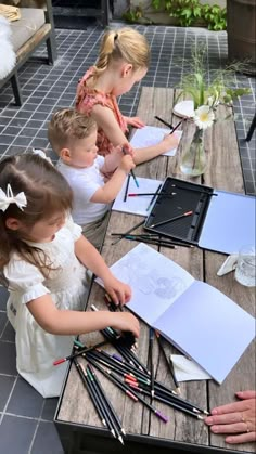 four children are sitting at a table with art supplies and watercolor pencils in front of them