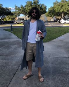 a man with long hair and beard standing on the sidewalk holding a bottle of water