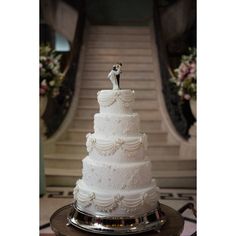 a white wedding cake sitting on top of a metal tray in front of a staircase