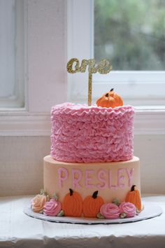 a cake with pink frosting and pumpkins on top is sitting in front of a window