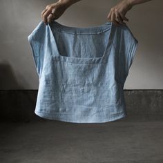 a person holding up a blue shirt in front of a white wall and cement floor