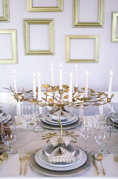 the table is set with plates, silverware and gold framed pictures on the wall