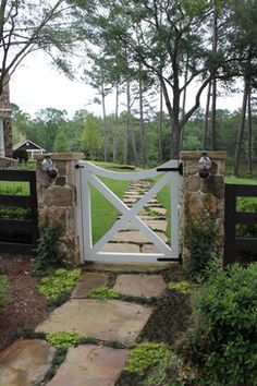 an open gate leading into a lush green yard with stone steps and trees in the background