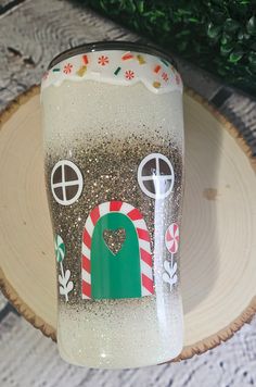 a glass with a house on it sitting on top of a wooden plate next to a christmas tree