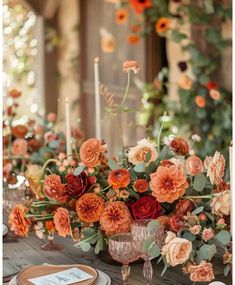 an arrangement of flowers and candles on a table with place settings in front of them