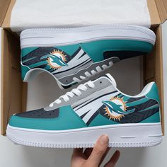 a pair of shoes with miami dolphins on them in a cardboard box, which is being held up by someone's hand