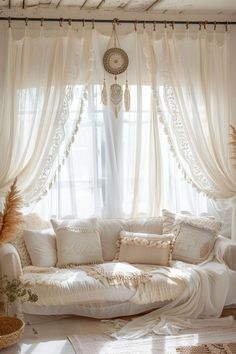 a white couch sitting in front of a window covered in sheer curtains and drapes