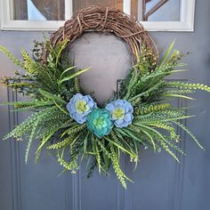 a wreath with blue flowers and greenery hangs on the front door's gray door