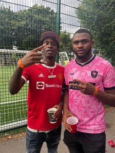 two young men standing next to each other holding cups and pointing fingers at the camera