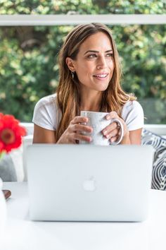 a woman sitting in front of a laptop holding a coffee mug