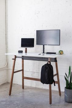 a computer desk with two monitors and a backpack on it, in front of a white brick wall