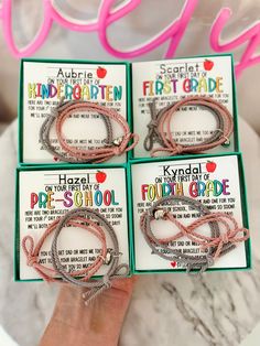 four packaged bracelets are shown in front of a marble table with pink and white letters