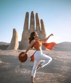 a woman in white pants and an orange top is dancing with her hands behind her