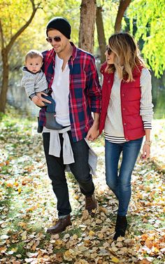 a man and woman walking through leaves with a baby