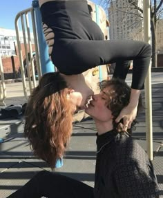 two women are kissing while sitting on the ground in front of a metal pole and some buildings