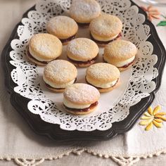 a plate full of cookies on a doily with some flowers in the back ground