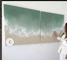 a woman is standing in front of two paintings on the wall and pointing at them