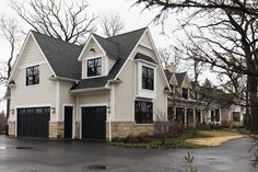 a large white house with black garage doors and windows on the top floor, surrounded by trees