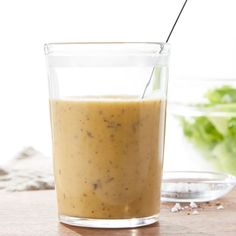 a glass filled with liquid sitting on top of a wooden table next to a salad