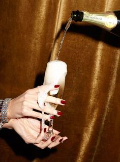 a woman's hand holding a wine glass and pouring it into a champagne bottle