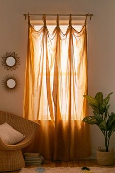 a living room with a chair, mirror and window covered in yellow sheer curtaines