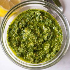 a glass bowl filled with pesto next to a lemon wedge