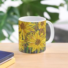 a coffee mug with sunflowers painted on it sitting on a table next to some books