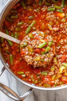 a pot filled with meat and vegetables on top of a marble counter next to a wooden spoon