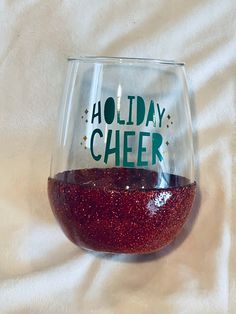 a red wine glass with the words holiday cheer on it sitting on a white sheet