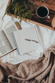 an open notebook and pen sitting on top of a bed next to a cup of coffee