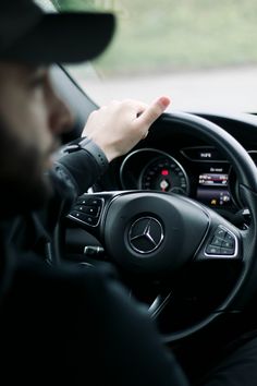 a man driving a car with his hand on the steering wheel and pointing at something