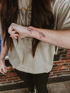 a woman with a tattoo on her arm holding onto another person's hand and looking at the camera