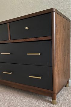 a black and brown dresser with brass handles on carpeted floor next to white wall