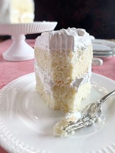 a piece of white cake on a plate with a fork next to it and another slice in the background