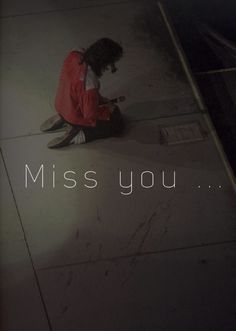 a person sitting on the ground in front of a sign that says, miss you