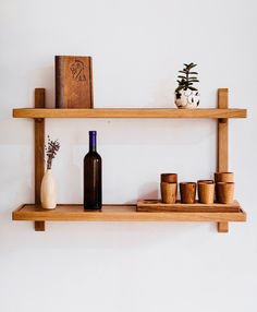 two wooden shelves with vases, cups and books on them against a white wall